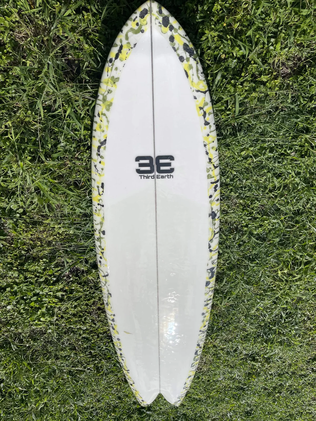 Full white Third Earth custom surfboard with yellow green and black splatter rails