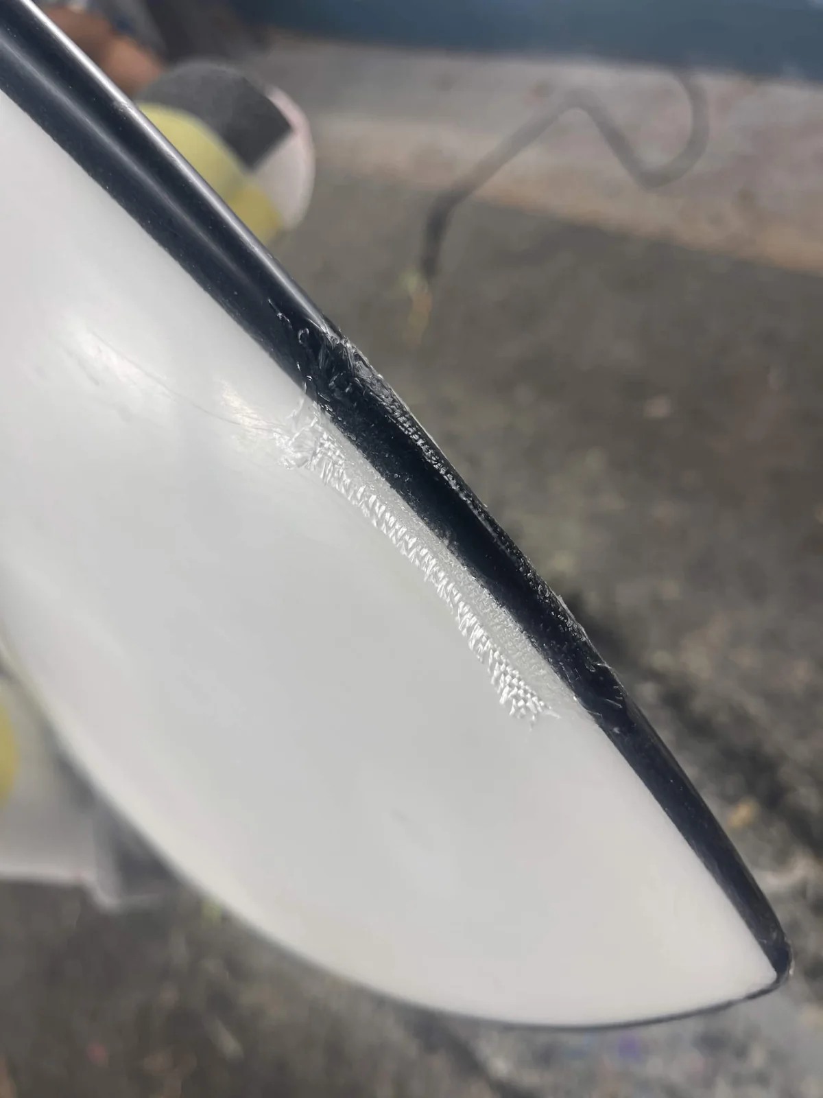 Fiberglass repair being laminated along a black surfboard rail